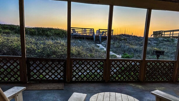 Un espacio de estar al aire libre techado con vista a la puesta de sol sobre la playa.