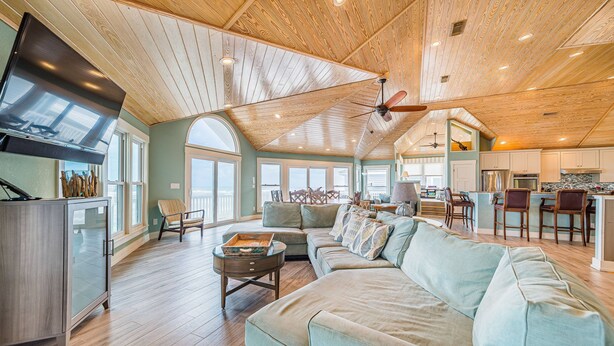 A spacious living area with a high ceiling, wooden beams, and a large window providing natural light.