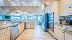 A spacious kitchen with wooden ceiling, granite countertops, stainless steel appliances, and a view to the outside.