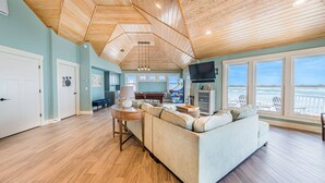 A spacious living room with a high ceiling, a large sofa, a dining area, and a kitchen.