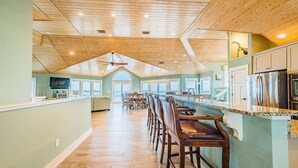 A spacious kitchen with a high ceiling, wooden beams, and a long bar area with bar stools.