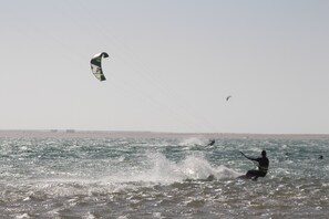 A beach scene with a person windsurfing and a kite in the sky.