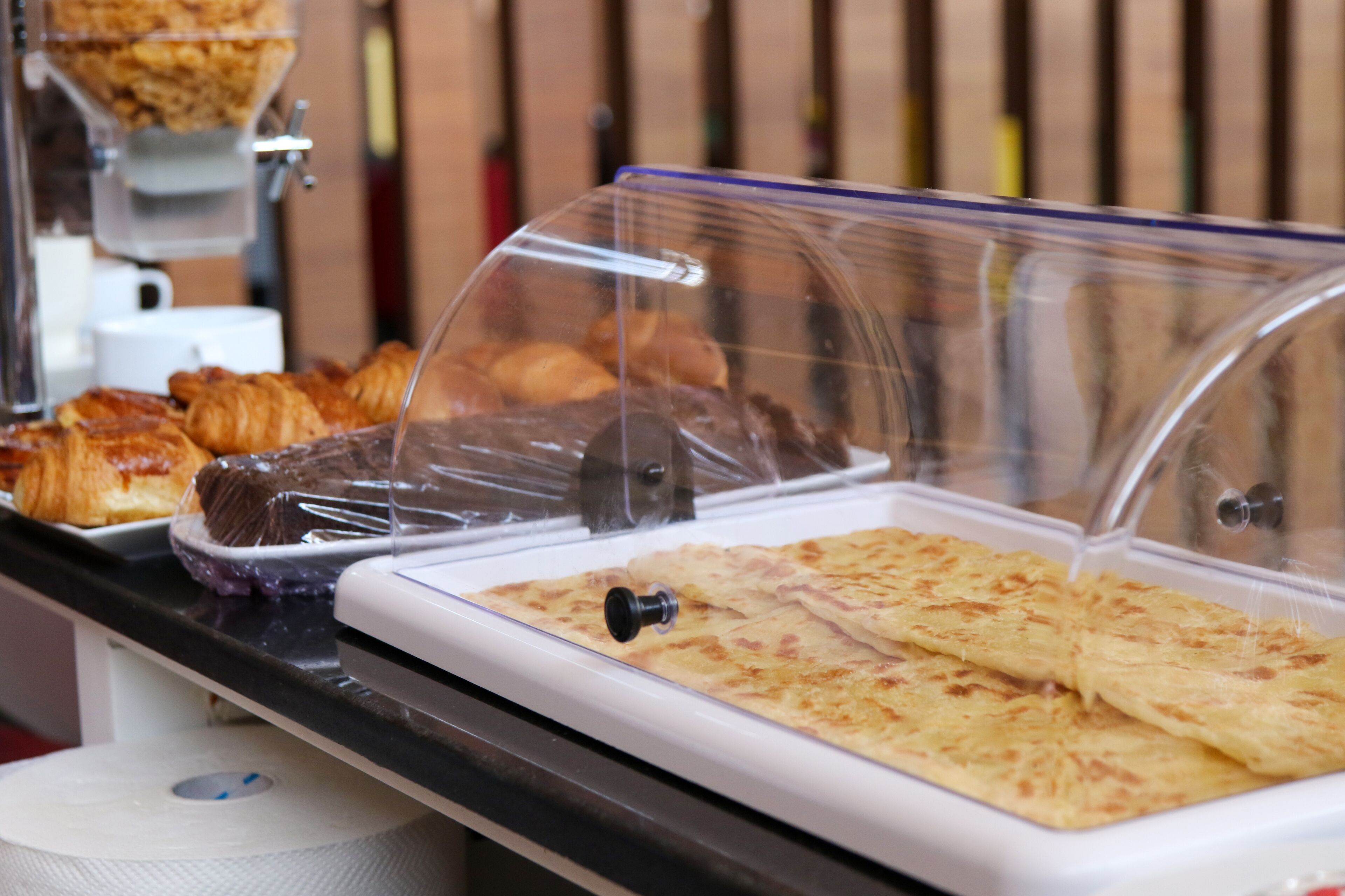 Un buffet della colazione con varie paste e prodotti da forno esposti in contenitori di plastica trasparente.
