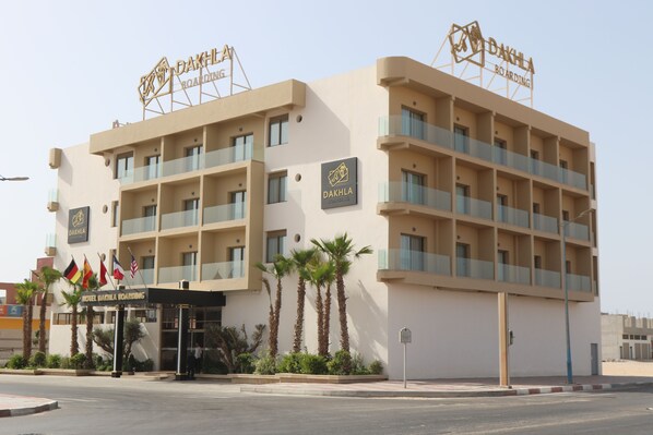 A multi-story hotel with balconies, palm trees, and flags.