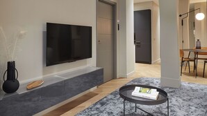A modern living room with a flat-screen TV mounted on the wall, a small round coffee table, and a dining area in the background. - Azoka Suite by FeelFree Rentals (Donostia)