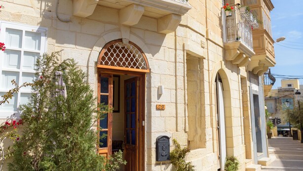 Un edificio histórico con fachada de piedra, puerta de madera y un balcón con barandillas metálicas.
