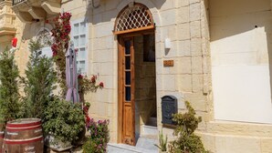 Un edificio de piedra tradicional con puerta de madera, un balcón con barandillas de metal y plantas en macetas.