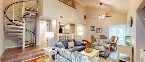 A spacious living room with a curved staircase, a dining area, and a kitchen in the background.