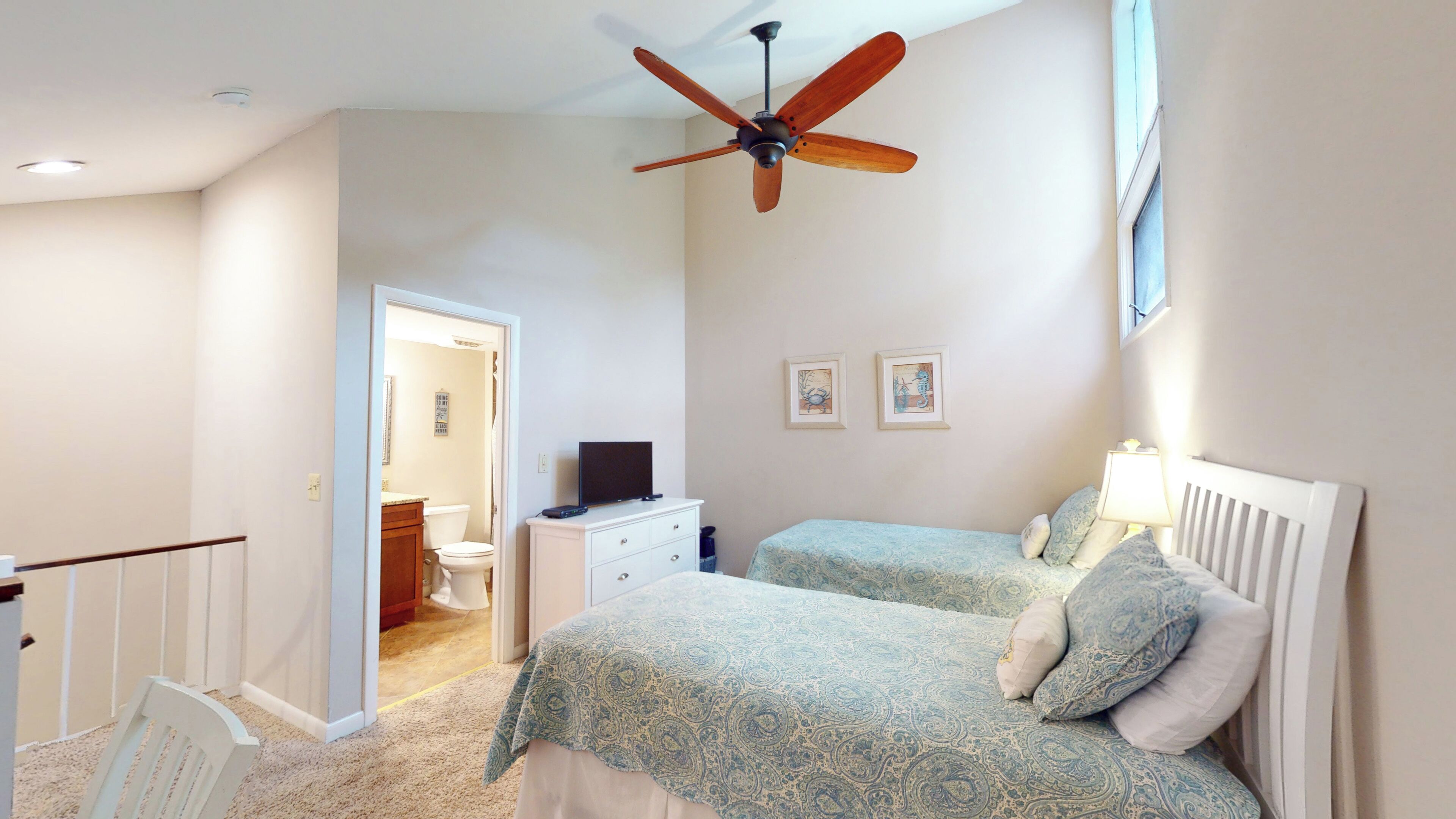 Une chambre avec deux lits, un ventilateur de plafond, une télévision et une salle de bain visible à travers une porte ouverte.