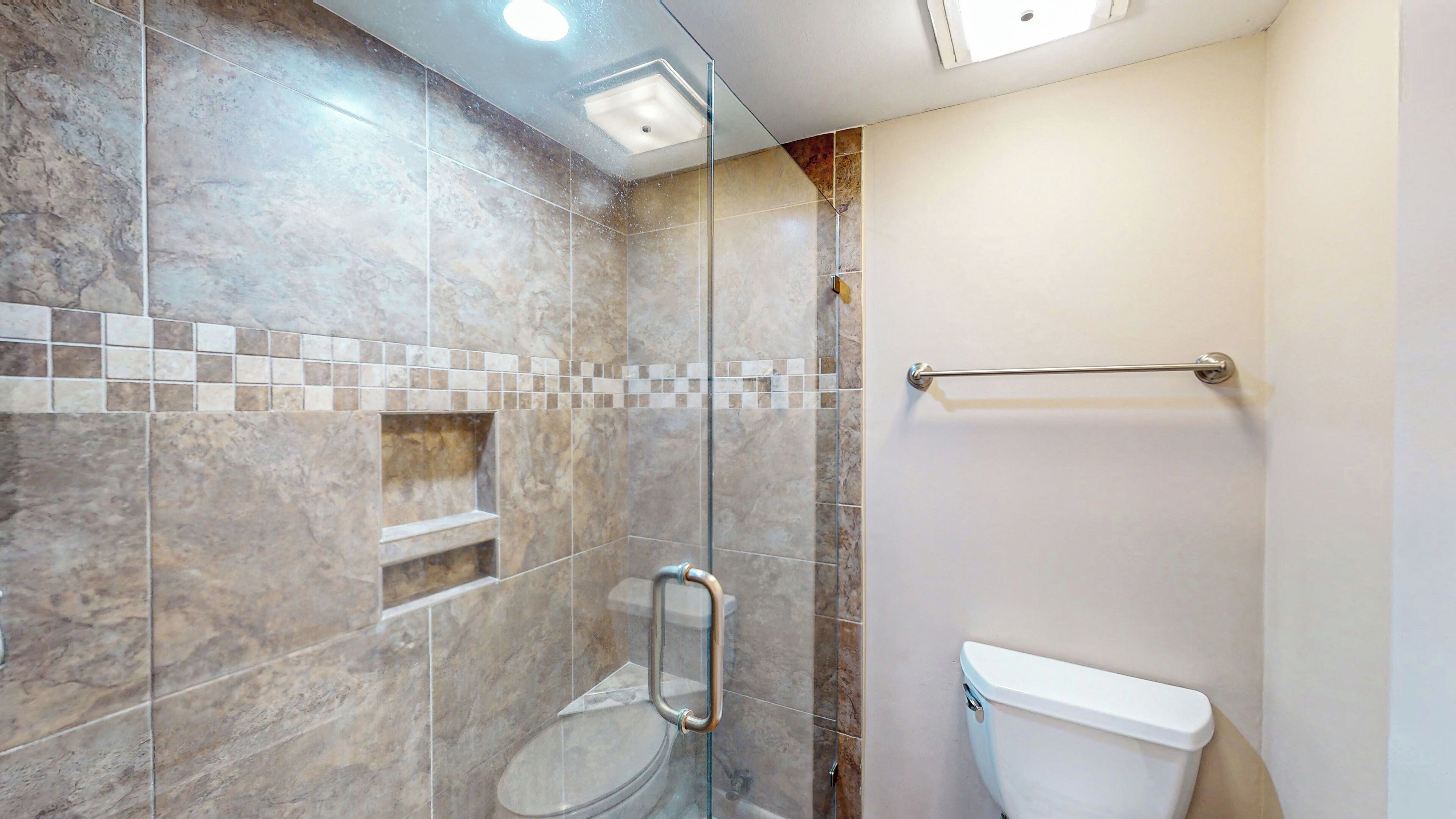 Un baño con cabina de ducha de vidrio, inodoro y estante.