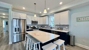 Una cocina moderna con armarios blancos, electrodomésticos de acero inoxidable, una isla grande con taburetes altos e iluminación colgante.