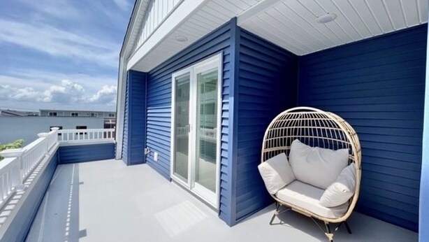Una casa azul con porche blanco, una silla de mimbre y una puerta de cristal.