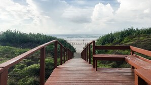 Een houten looppad leidt naar een strand met uitzicht op de oceaan en een bewolkte lucht.
