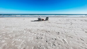 Een strand met een rolstoel en een stoel, een heldere lucht en de oceaan op de achtergrond.