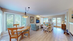 Ein geräumiges Wohnzimmer mit Essbereich, Holzböden und großen Fenstern mit Jalousien.