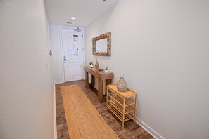 A hallway with a wooden floor, a bench, a mirror, and a small table with a vase. - Book Chillaxin 214B | Sandbridge Vacation Rental | Ocean Sands Realty (Virginia Beach)