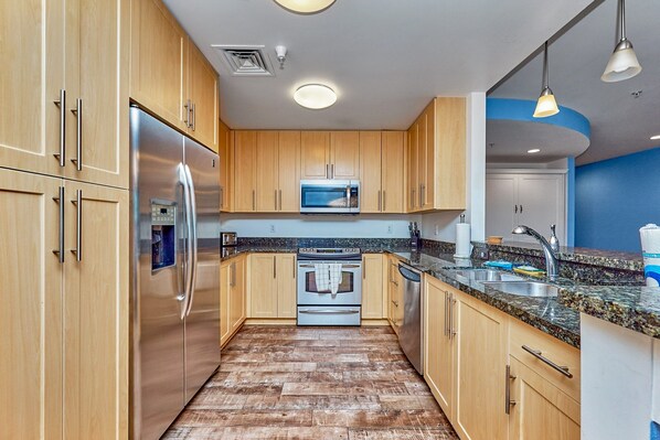 A modern kitchen with wooden cabinets, stainless steel appliances, granite countertops, and a wooden floor. - Book Chillaxin 214B | Sandbridge Vacation Rental | Ocean Sands Realty (Virginia Beach)