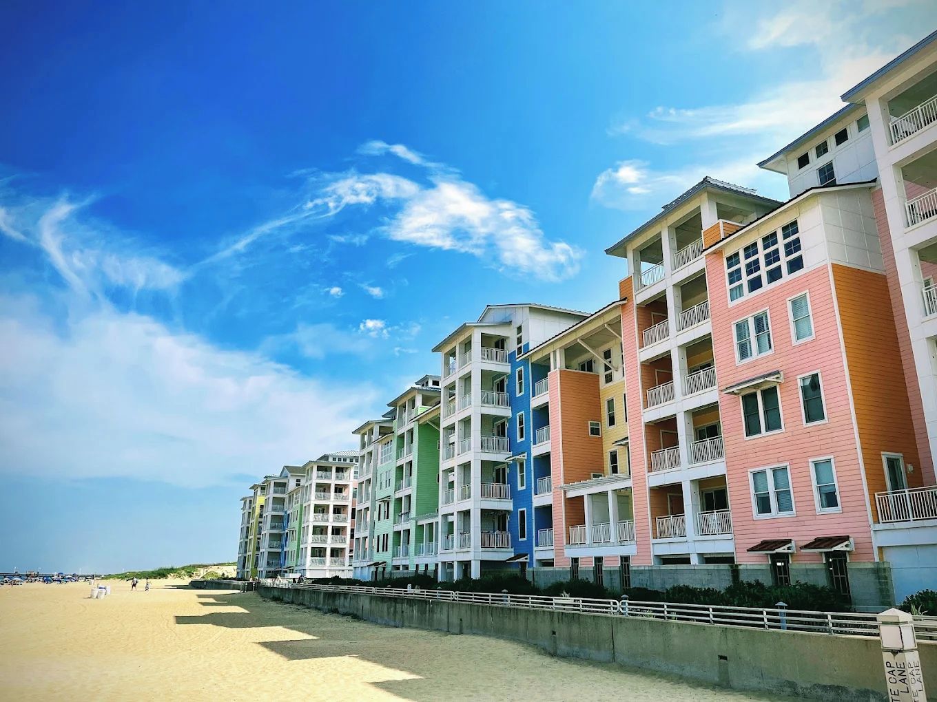 A beachfront hotel with multiple colorful buildings, a sandy beach, and a clear sky.