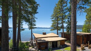 A lakeside cabin with a deck and a covered patio, surrounded by tall trees and a clear view of the lake. - Star Harbor # 06 by Hauserman Rentals (Tahoe City)