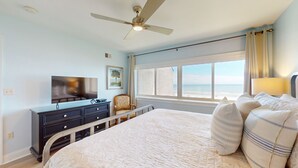 Une chambre à coucher avec un lit, une télévision, une chaise et une fenêtre donnant sur la plage.