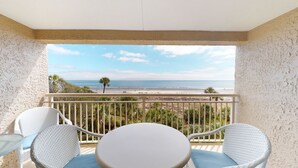 Un balcon avec vue sur la plage, des meubles en osier blanc et une petite table.