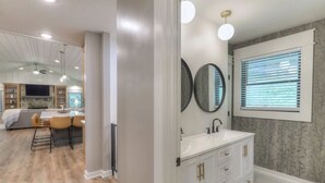 Une salle de bain moderne avec un meuble-lavabo blanc, un grand miroir et une fenêtre équipée de stores.