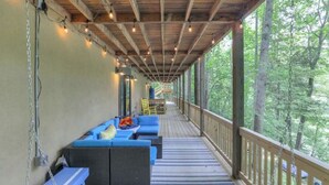 Une terrasse extérieure couverte, dotée de sièges bleus, de rampes en bois et de guirlandes lumineuses.