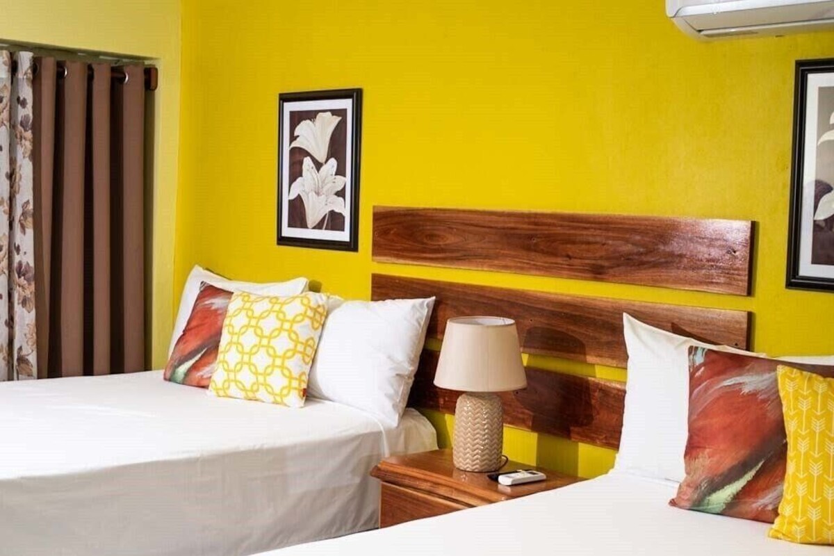 A hotel room with two beds, a wooden headboard, a nightstand with a lamp, and a framed picture on the wall.