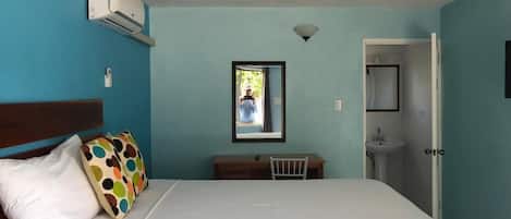A bedroom with a bed, a desk, a chair, an air conditioning unit, and a bathroom.