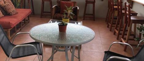 A patio with a round glass table, chairs, a sofa, and a view of greenery outside.