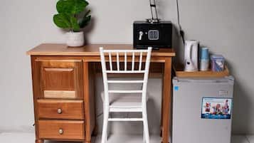 Un escritorio de madera con una silla blanca, una radio pequeña negra y un refrigerador compacto.