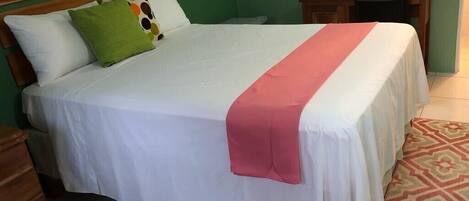 A neatly made bed with a white bedspread and a pink blanket, a wooden headboard, and a green wall.