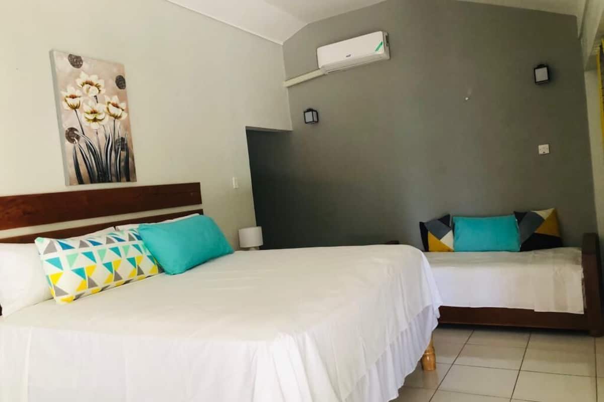 A hotel room with two beds, a painting on the wall, an air conditioning unit, and a nightstand with a lamp.