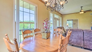 A dining area with a wooden table and chairs, a chandelier, and a view through large windows. - 'Angler's Ridge' Waterfront Family Getaway! (Mammoth Spring)