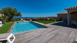 Una piscina con cubierta de madera, sillas de descanso y vista al mar.