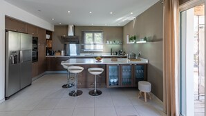 Una cocina moderna con una isla central, taburetes de bar, horno empotrado y un amplio ventanal.