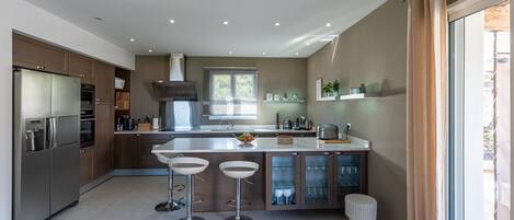 A modern kitchen with a central island, bar stools, a built-in oven, and a large window.