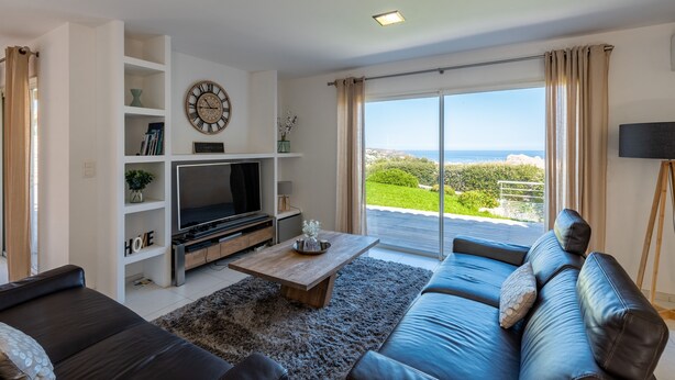 Un salón moderno con un televisor de pantalla plana grande, una mesa de centro de madera, un sofá y vistas al exterior.