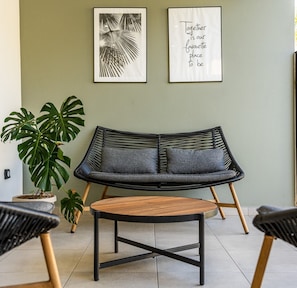 Un salon moderne avec un canapé noir, deux œuvres d’art encadrées, un monstera en pot et une table basse en bois.