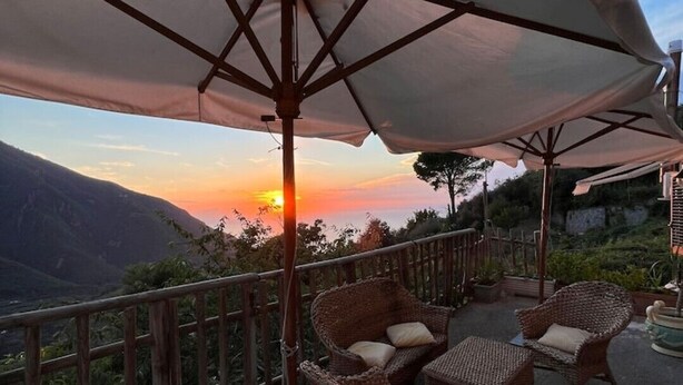 Eine Terrasse mit Korbmöbeln und einem großen Sonnenschirm, mit Blick auf einen malerischen Sonnenuntergang.