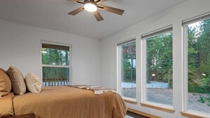 Ein Schlafzimmer mit einem Bett, einem Deckenventilator, großen Fenstern und Blick ins Freie.