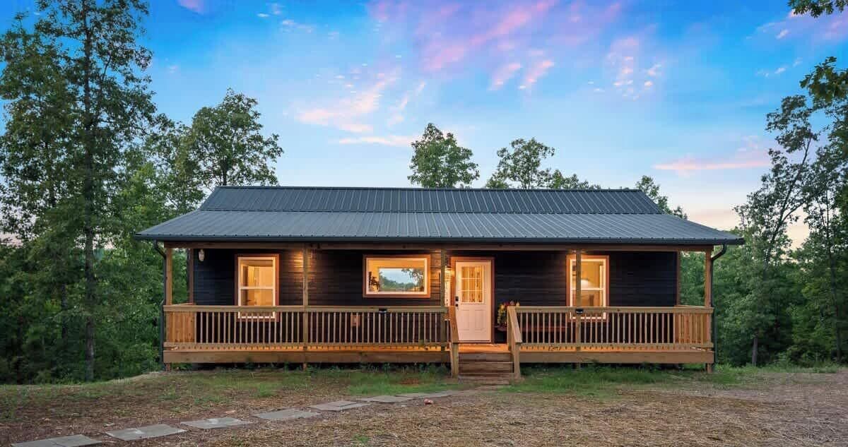 A cabin with a wooden deck, a porch, and a metal roof.