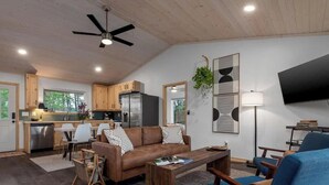 Eine moderne Küche mit Holzausbau, ein Essbereich mit Tisch und Stühlen, ein Wohnzimmer mit Sofa und Couchtisch sowie ein Flachbildfernseher an der Wand.