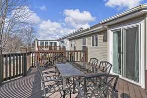 Eine Terrasse mit einem Tisch und Stühlen mit Glastisch, einem Holzwert und einer Glasschiebetür zu einem Haus.