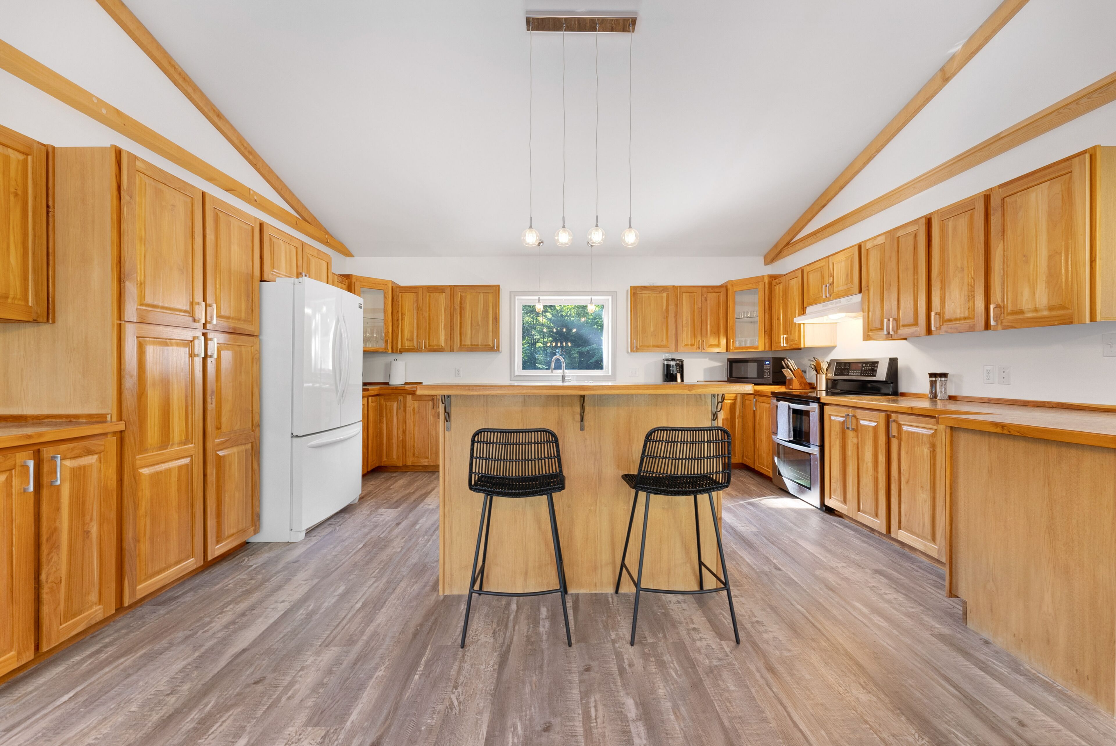 A modern kitchen with wooden cabinets, a white refrigerator, a built-in oven, and a large window.