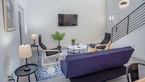 A modern living room with a sofa, two chairs, a coffee table, and a TV mounted on the wall.