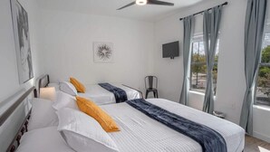A hotel room with two beds, a ceiling fan, a TV, and a window with curtains.