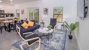 A modern living room with a sofa, two chairs, a coffee table, and a TV mounted on the wall.