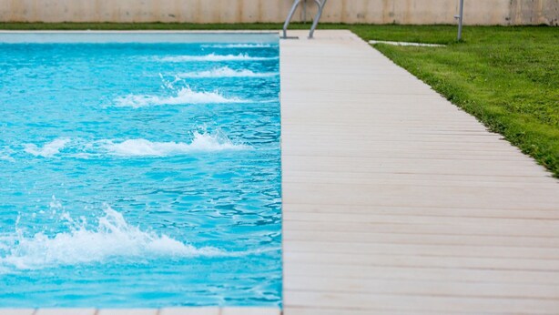 Ein Schwimmbecken mit Holzterrasse und Metallleiter.