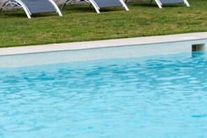 A swimming pool with clear water, surrounded by a grassy area and white poolside chairs. - H. Nomad Suite - One Room Hotel, Sleeps 2 (Vejer de la Frontera)
